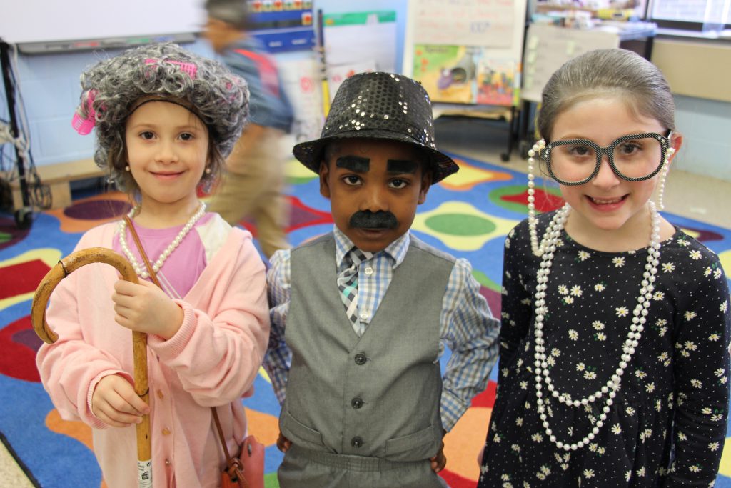 Three kindergarten students are dressed as old people. One boy in the center and two girls on either side..