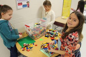 Students stand around a table with lots of Legos building things.