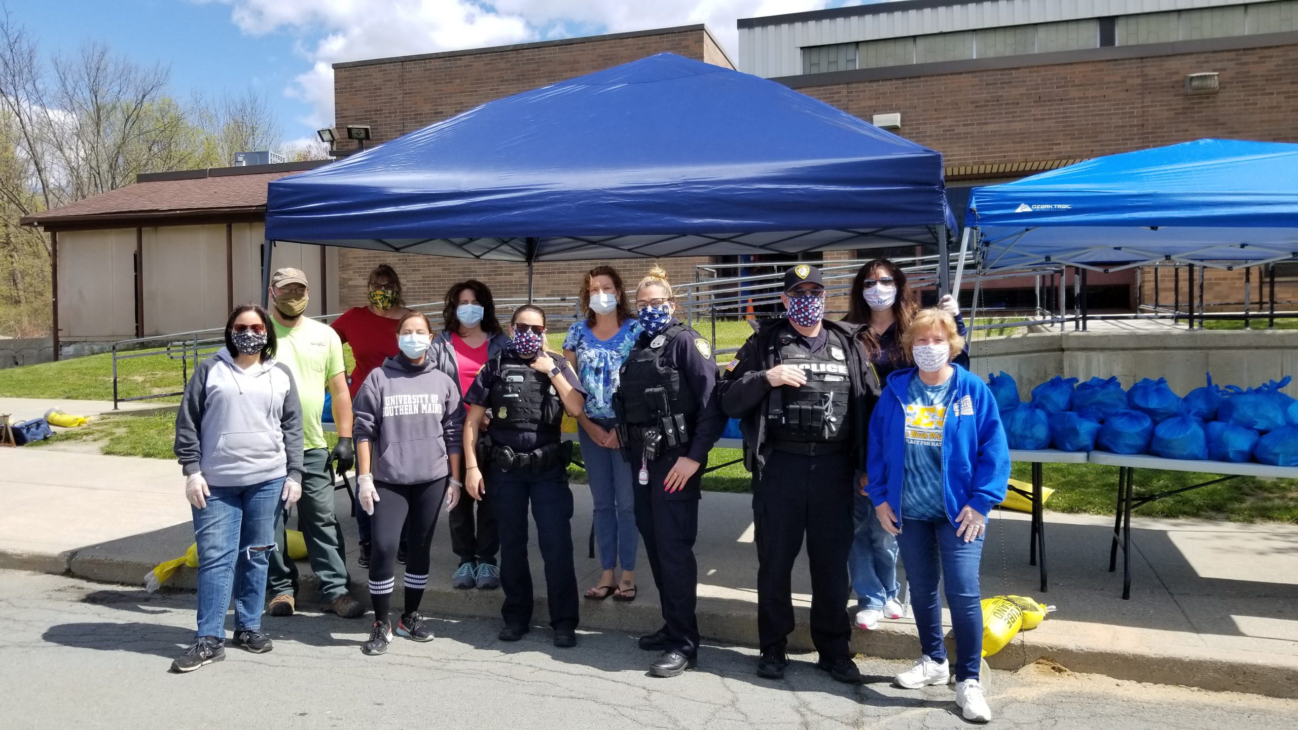 a dozen people with masks on stand in front of a blue tent