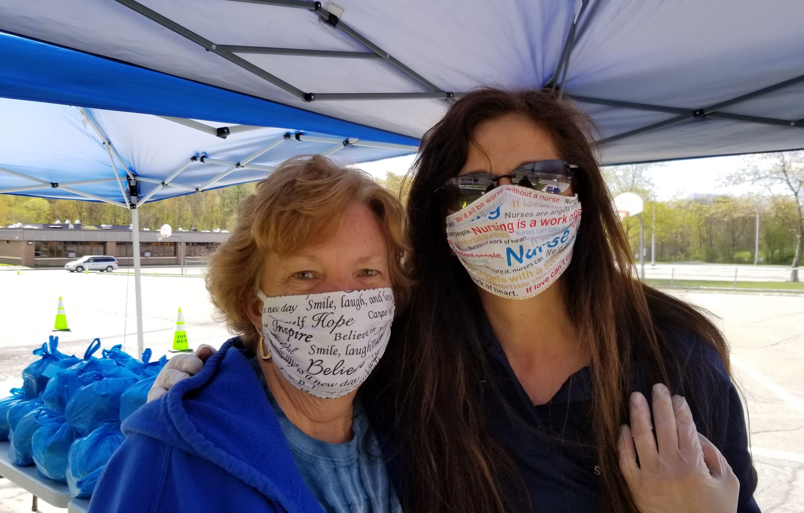 Two women wearing protective face masks and standing under a blue tent.