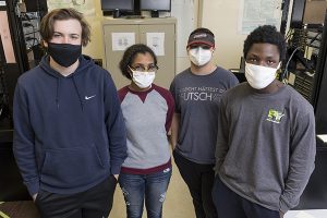 Four high school students , all wearing masks, stand shoulder to shoulder.