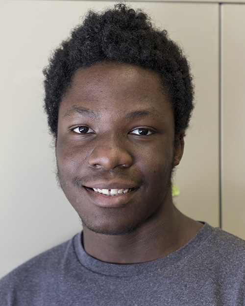 A Black male high school student with short black hair is smiling.