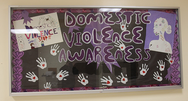 A bulleting board with a black background and the words Domestic Violence Awareness in purple. There are cutouts of hands all around it with hearts on the palms. 