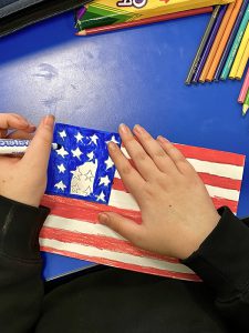 A blue desk with a drawing of a flag with a girls hands coloring it.