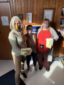 Three women stand together with arms around each other. All are wearing masks.