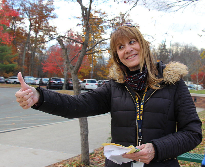 A woman with longish blonde hair, wearing a blue winter jacket, gives a thumbs up and is smiling broadly.