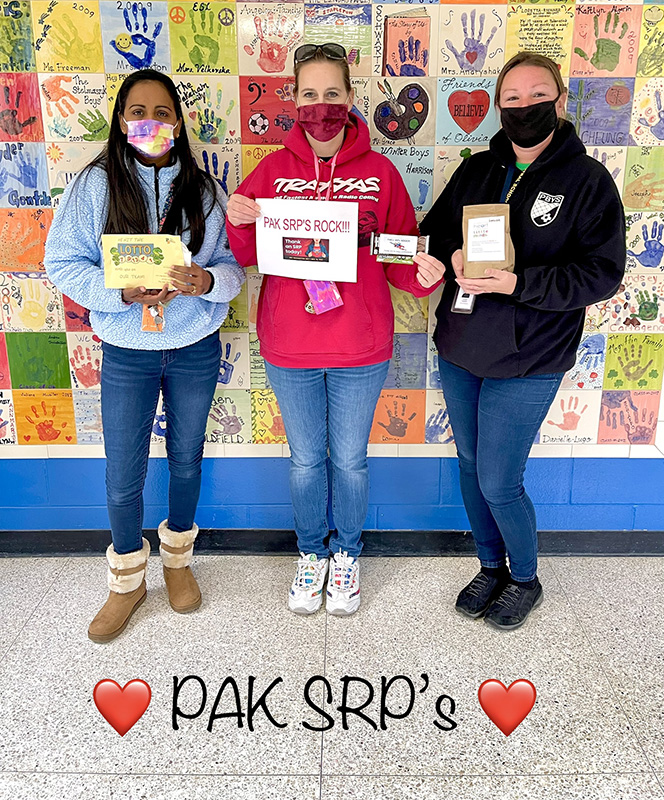 Three women stand in front of a wall painted with all different color  squares painted. They are all masked and holding certificates. Across teh bottom says PAK SRPs with hearts.