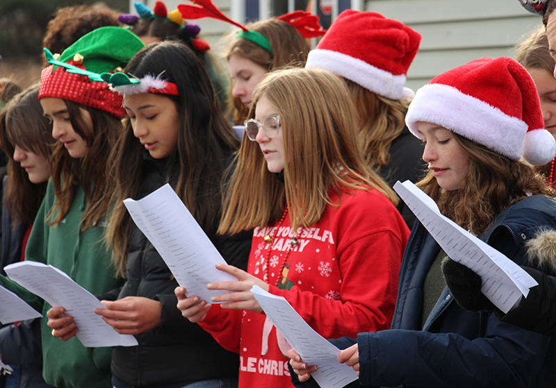 A group of middle school students stand together and sing. They are dressed in festive hats.