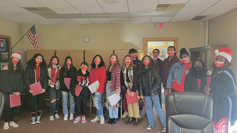 A group of high school students dressed in festive red and plaid, all wearing red masks.