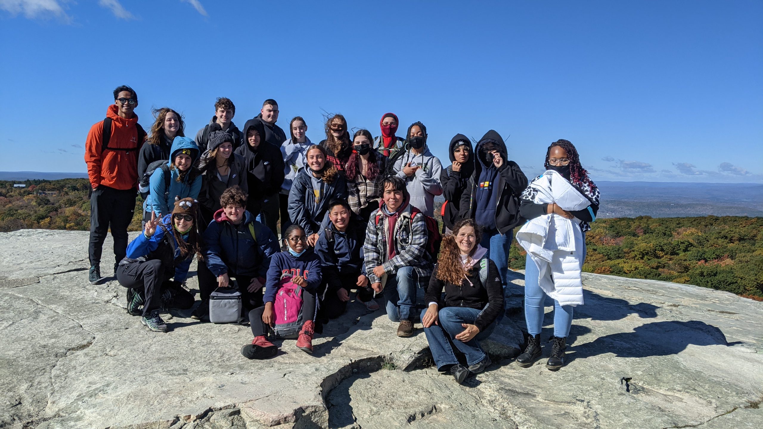 A group of about 20 high school students standing on a large rock at an overlook. The sky is right blue behind them.