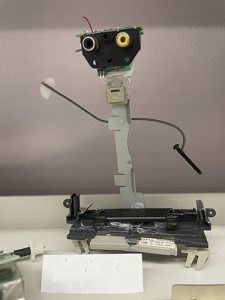 A little sculpture using old electronic parts. It looks like a robot with two arms and eyes.