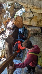 The view is from above. High School students walk down between large rock walls. The space they are entering is very  narrow.