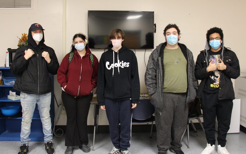 Five high school students stand next to each other. They are all wearing masks.