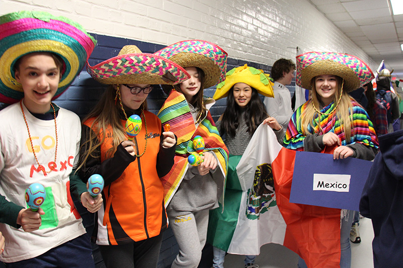 Five middle school students dressed in traditional Mexican garb, with sombreros and ponchos. One is holding a sign that says Mexico