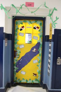 A classroom door decked out in yellow and blue like the flag of Panama There are green decorations all around the door.