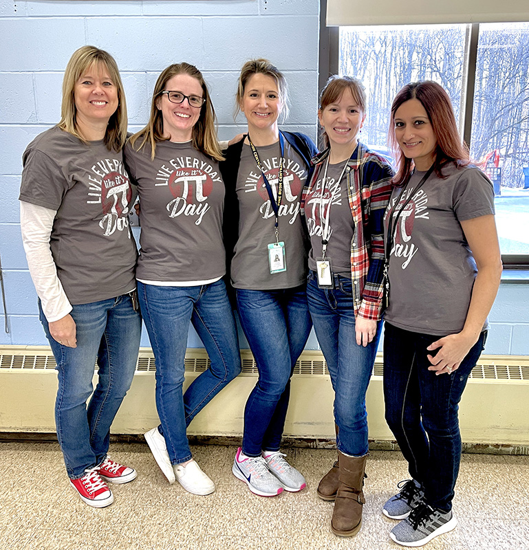 Five women all wearing gray shirts with the pi symbol on it.