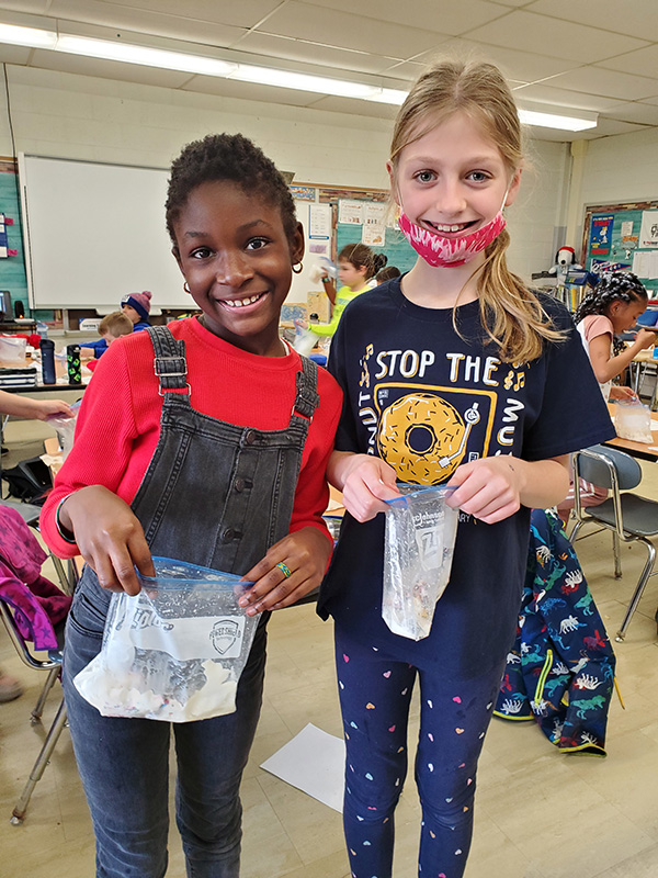 Two girls smile and hold plastic bags that contain homemade ice cream.