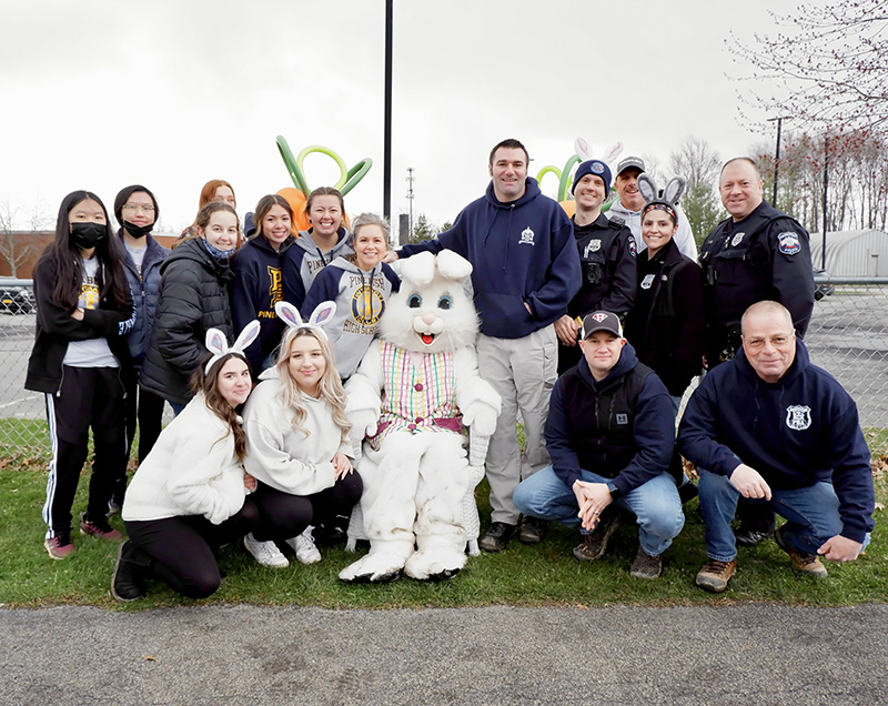 A group of high school students and adults pose together with a large costumed Easter bunny.