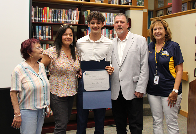 A group of five people, three women, a man and a young man who is holding a certificate. They are all smiling.