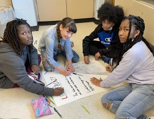 Four fifth-grade students are on the floor creating a poster about leadership.