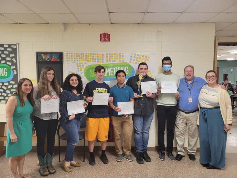 A group of six high school students stand together all holding certificates. There is a woman on the left and a man and woman on the right.