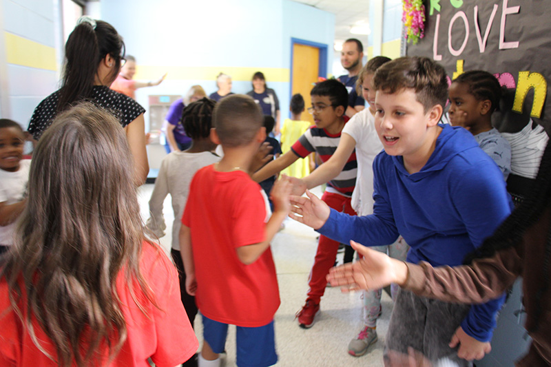 A group of younger elementary students walk past older kids who are high fiving them.