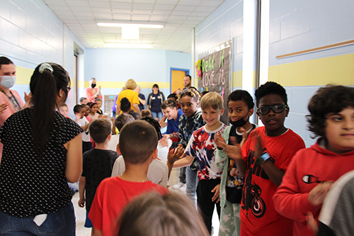 ELementary students line a hallway and clap and congratulate a parade of elementary students walking past them.