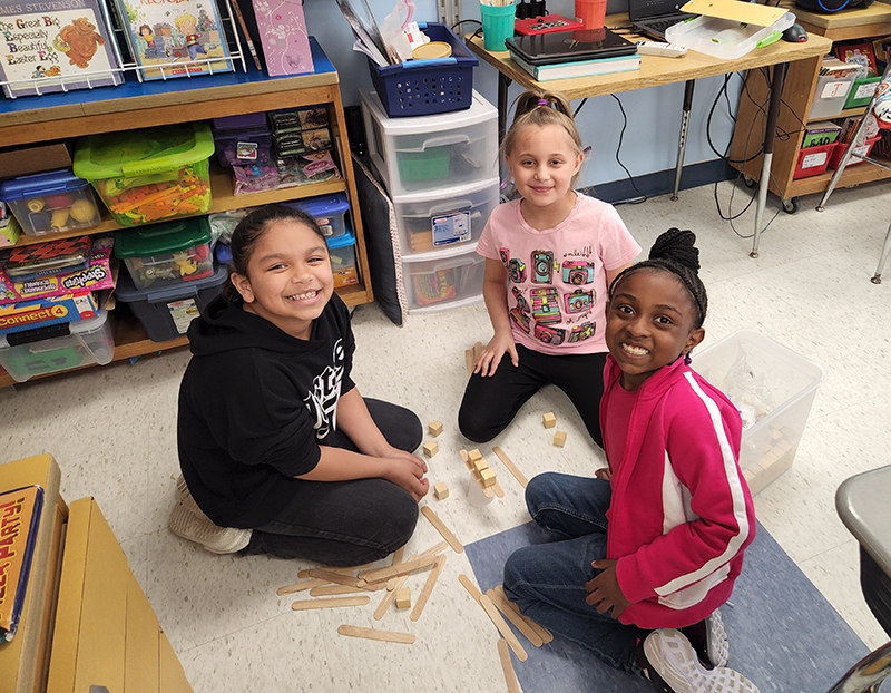 Three second-grade girls sitting on the floor with blocks they are building with.