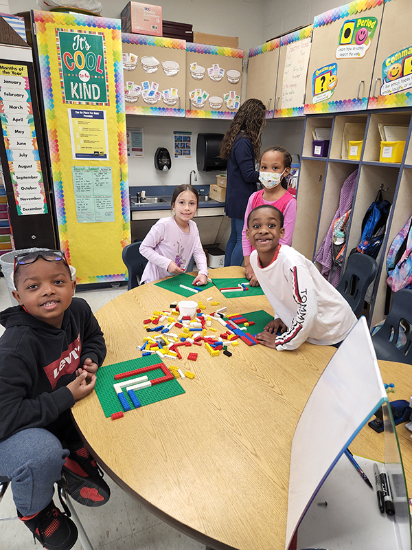 A group of four econd-grade students at a table with lots of blocks. They are smiling.