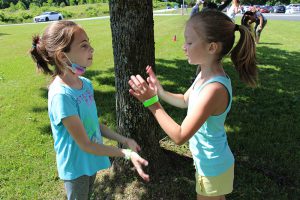 Two girls dressed in summer shirts and shorts play a game together where they slap their hands.