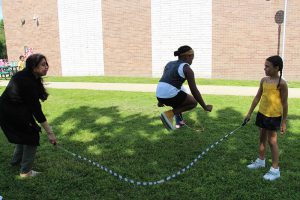 A woman and an elementary-age girl hold the ends of a long jump rope as a girl jumps it.