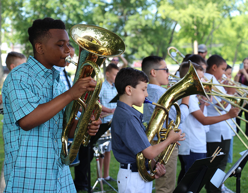 A row of fifth-grade boys play brass instruments.