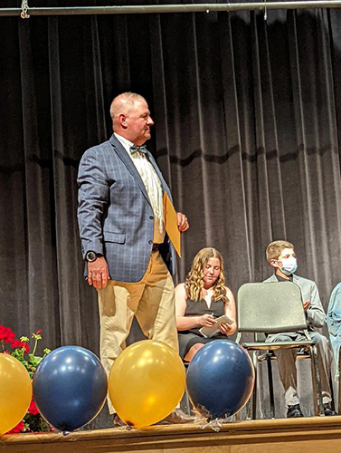 A man wearing a blue jacket, khaki pants and bow tie walks across the stage.