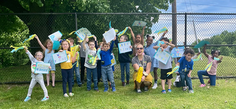 A group of kindergarten students holding signs up in the air.