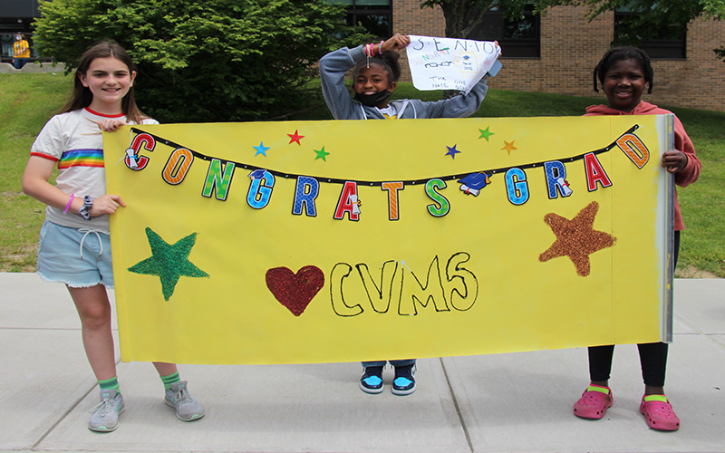 Three middle school students hold a yellow sign that says Congratulations CVMS