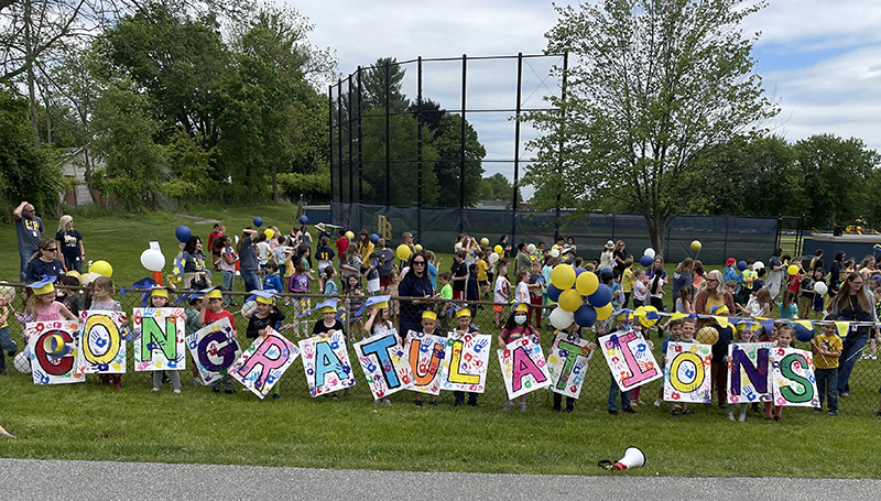 A large group of elementary students stand in a line holding signs that spell out congratulations.