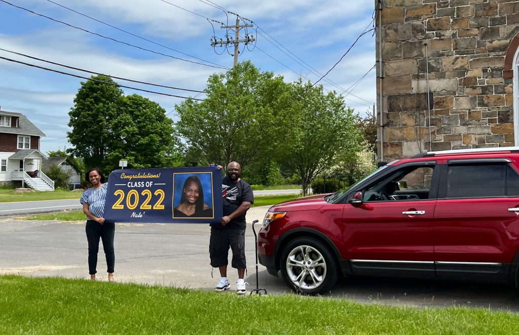 A man and woman hold a large banner that says class of 2022 with a big picture on it of a graduating girl.