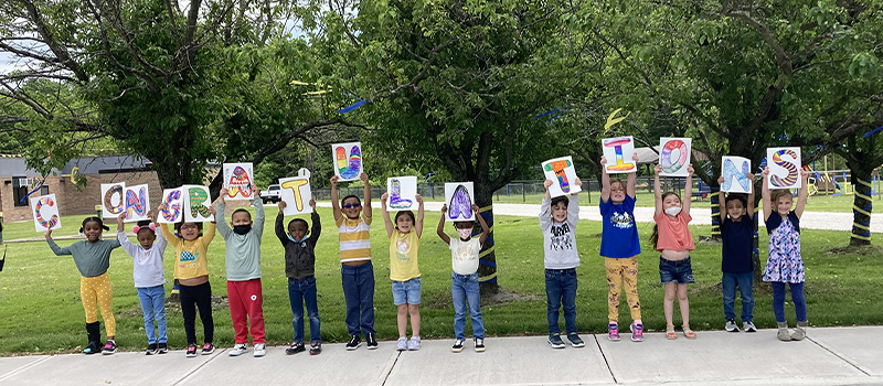 Smaller elementary students hold signs up over their head that spell out Congratulations