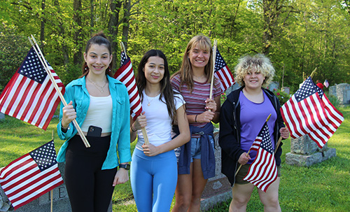 Four middle school girls stand together smiling. Each is holding an American flag.