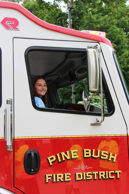 A fifth-grade girl smiles as she looks out of a window of a fire truck that says Pine Bush Fire District.