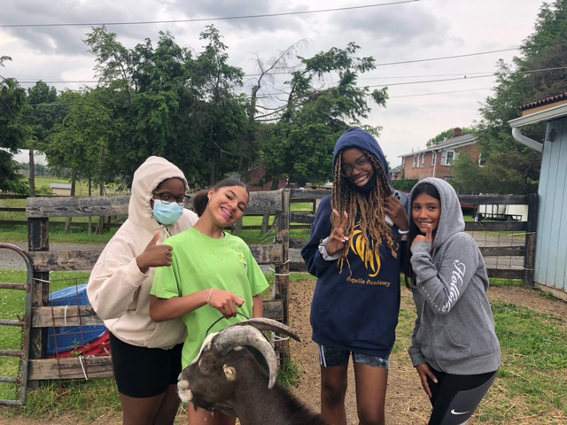 Four middle school students smile outside with a dark goat.