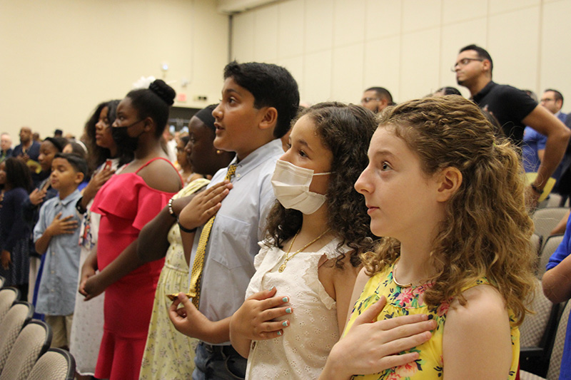 A line of students stand with their hands over their hearts.