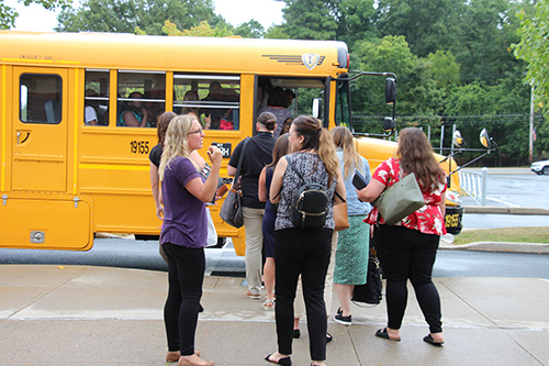 A group of adults board a yellow school bus. There are many people already on the bus.