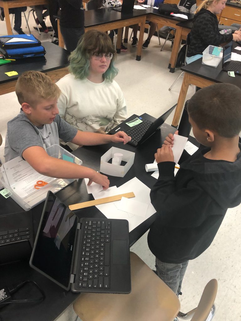 A group of three middle school student sworking on building a tower made of index cards.