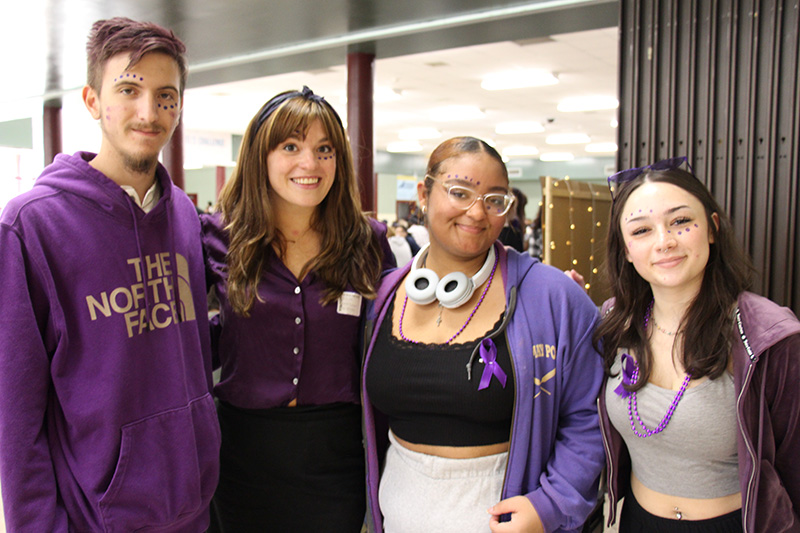 Four people stand arm in art and smile. They are all wearing purple. 