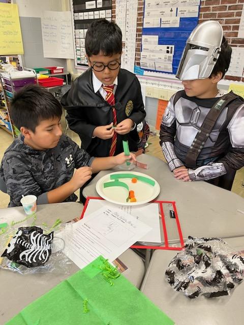 A group of three elementary age boys, dressed in costumes, work on a science experiment together.