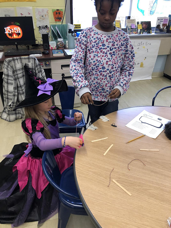 Two elementary students work together at a table . They are dressed in costumes.