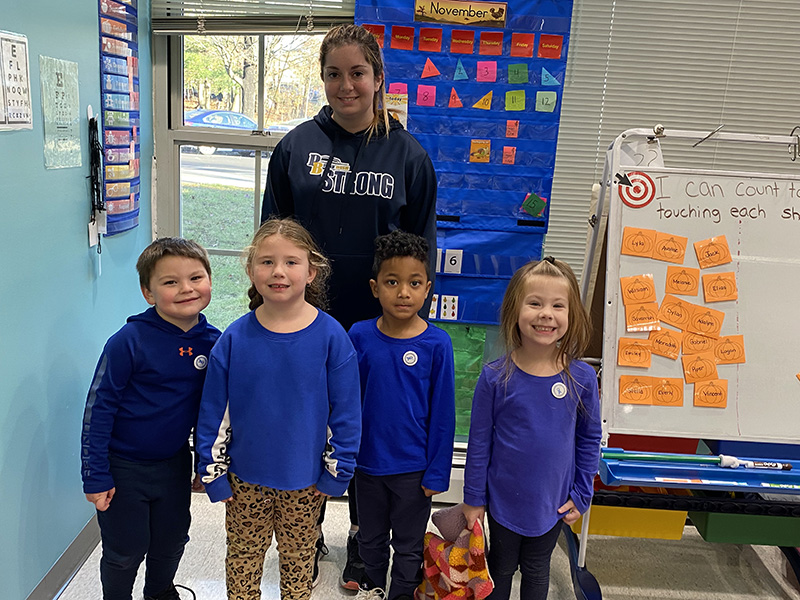 A group of four pre-K students with their teacher standing behind them, all dressed in blue.