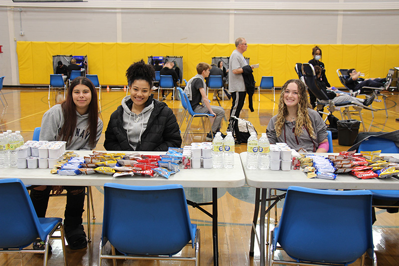 Three high school girls sit at a table filled with snacks.