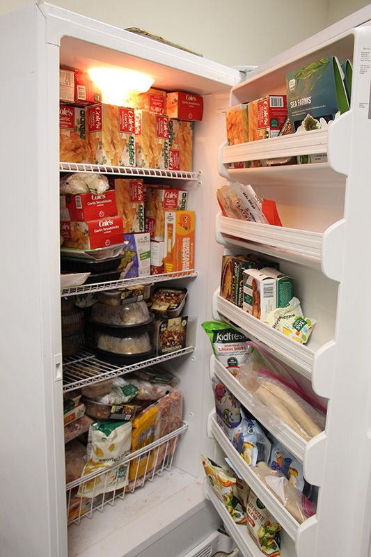 A freezer is open and stocked with food items. It is full.